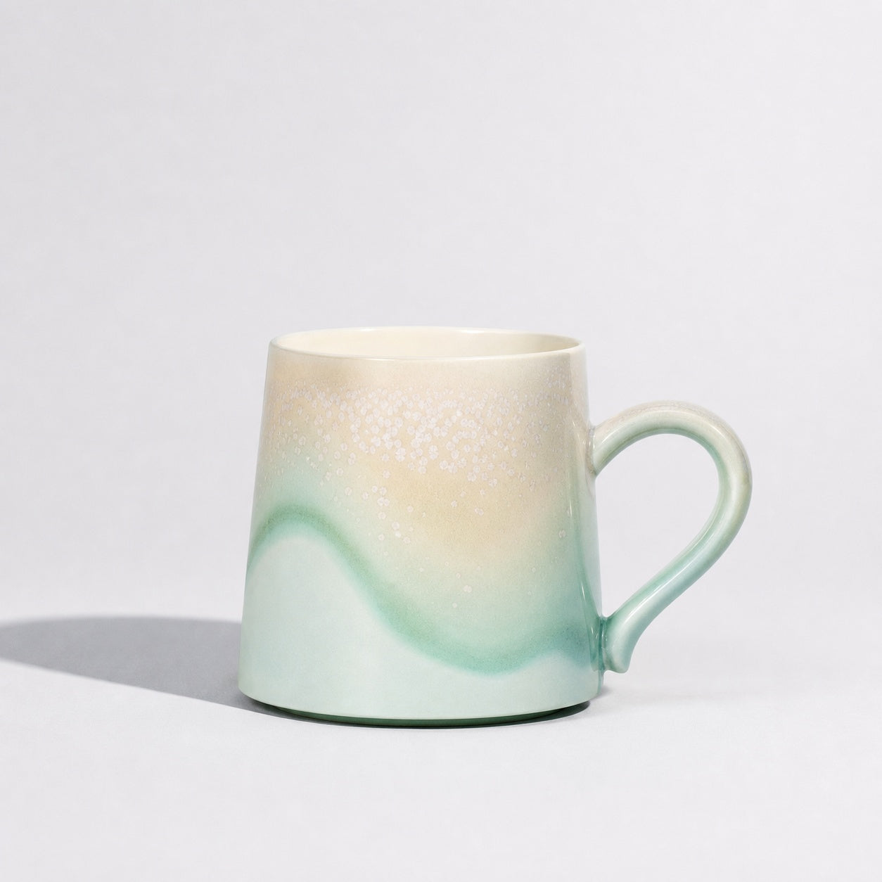 Pastel green mug with an ivory wave glaze and curved handle